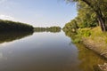 Wide yellow river is slow flowing. Early autumn. Sunny weather and brightgreen trees on the banks fron the both sides