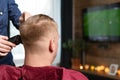 Wife cutting husbands hair at home indoors in front of TV with clipper and holding comb in other hand Royalty Free Stock Photo