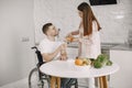 Wife encourage disabled husband sitting in wheelchair at kitchen table Royalty Free Stock Photo