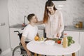 Wife encourage disabled husband sitting in wheelchair at kitchen table Royalty Free Stock Photo