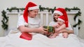 Wife and husband give gifts to baby on bed decorated for christmas an