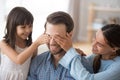 Wife with kid closing eyes of smiling daddy make surprise