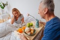 Wife looking at husband holding tray with breakfast and flowers Royalty Free Stock Photo