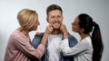 Wife and senior mother pinching young man cheeks, overprotection in family Royalty Free Stock Photo