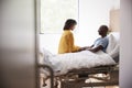 Wife Visiting And Talking With Patient Husband In Hospital Bed