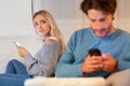 Wife Watching Husband Chatting On Cellphone Sitting On Couch Indoor