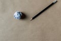 A wihte paper ball and black pencil on brown paper background.