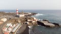 Wild black sand beach with cave and small boats and a port with lighthouse in volcano coastline. Volcanic soil in rural village in Royalty Free Stock Photo