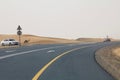 A wild camel walks on a road next to a desert in Dubai UAE as cars drive past