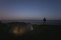 Wild camping with a tent at night in summer. A man stands with a headlamp on the edge of a sea cliff in Paldiski. Starry sky