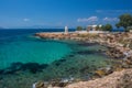 The wild coast of Aegina island with clear and blue waters of Mediterranean sea and the old small lighthouse in the background, in