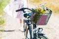 Wild flowers bouquet in basket of bicycle with woman in flowery dress in background, bike with flowers in field in summertime