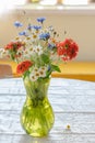 Wild flowers bouquet in the green glass vase on the table with white tablecloth in the natural light, Royalty Free Stock Photo