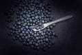 Wild forest blueberries and white ceramic spoon piled on black table cover darkened background