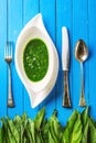 Wild garlic leaves with garlic soup in white plate and cutlery on blue wooden background, healthy lifestyle, seasonal spring herb Royalty Free Stock Photo