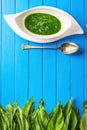 Wild garlic leaves with spoon and garlic soup in white plate on blue wooden background, healthy lifestyle, seasonal spring herb Royalty Free Stock Photo