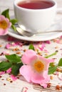 Wild rose flower and cup of tea on old rustic wooden background