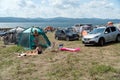 Wild vacation in a tourist camp with tents and cars in a big meadow on the shore of the Big Lake