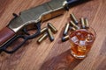 Wild west rifle and ammunitions with glass of whisky and ice on wooden table