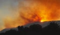 Wildfire on a mountain slope at sunset with dramatic red sky and heavy smoke