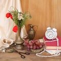 Wildflowers, red poppies in an old brass jug on an old wooden table, alarm clock, books, grapes, silk drapery, concept of time, Royalty Free Stock Photo