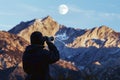 wildlife observer with binoculars, moon above mountain terrain