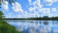 Willow branches overhang the grassy bank and the river. There are ripples on the water, in which the trees and the blue sky with c Royalty Free Stock Photo