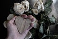 wilted rose flowers and a heart symbol in hand, the concept of a broken heart