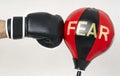 Win the fear concept with a strong man`s hand in a boxing glove hits the punching bag with text Fear