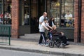 A young boy pushing an elderly lady in a wheelchair past shop windows