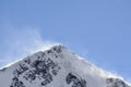 The wind blows snow from the snowy peak.