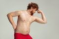 Cute red-headed man in red swimming shorts posing isolated on gray studio background. Concept of sport, humor and body