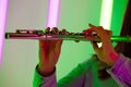 Wind instrument flute close up. Female hands hold a flute against the background of bright neon lights in a dark studio