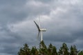 Wind power station standing among trees against a dark cloudy sky Royalty Free Stock Photo