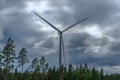 Wind power station standing among trees against a dark cloudy sky Royalty Free Stock Photo