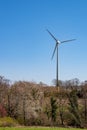 Wind turbine against blue sky, blooming wild cherry tree and and fields in foreground Royalty Free Stock Photo