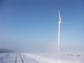 Wind turbine in misty snowy landscape against blue sky Royalty Free Stock Photo