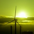 Wind turbine and power plant backlit at sunrise Royalty Free Stock Photo