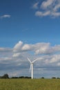 A wind turbine producing clean sustainable electricity in a field against a blue cloudy sky