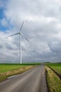 Wind turbines against a cloudy sky standing in a green field with a tarmac road