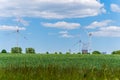 Wind turbines and electric power plant with smoking chimney in beautiful landscape with lush green agricultural wheat field. Royalty Free Stock Photo