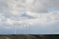 5 wind turbines spinning in the wind on a hill on a cloudy day