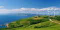 Wind turbines stand atop lush green hills with a panoramic view of the coast and sea, symbolizing sustainable energy generation Royalty Free Stock Photo