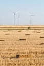 Wind turbines standing in rye field with bales of hay on foreground Royalty Free Stock Photo