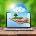 Wind turbines with tree in female hand in laptop Royalty Free Stock Photo