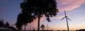 Wind turbines and trees form silhouettes against colorful sunset Royalty Free Stock Photo