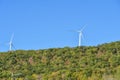 Wind turbines on a wooded hill and blue sky.