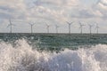 Wind and wave energy. Breaking waves with offshore windfarm turbines background