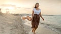 Wind whips woman\'s scarf as she joyfully dances and runs on the sandy beach at sunset. Highlights the concepts of fun, Royalty Free Stock Photo