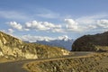 A winding asphalt road in the desert mountains against the snowy peaks under a blue sky with white clouds Royalty Free Stock Photo